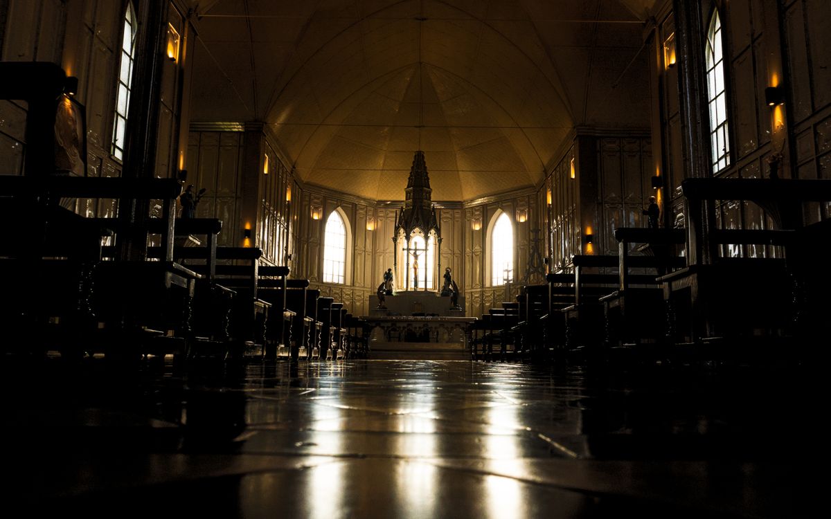Dramatic view of a gothic cathedral interior with rows of benches and altar.
