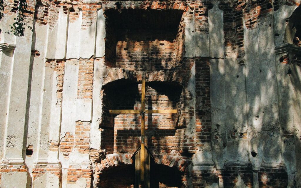 A wooden cross set against a historic brick wall with sunlight and shadows falling on it.