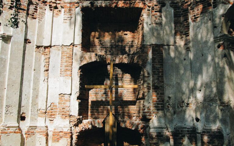 A wooden cross set against a historic brick wall with sunlight and shadows falling on it.