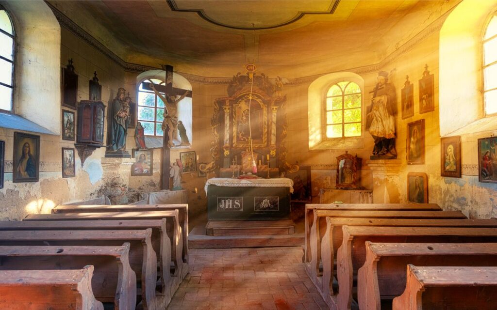 Interior of aged catholic cathedral with wooden seats icons and bright rays of sun shining through window