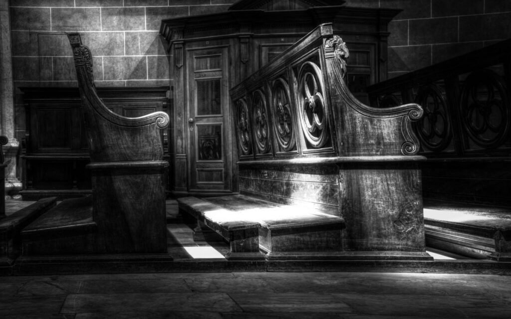 Intricate wooden church pews illuminated in monochrome lighting, showcasing sacred architecture.