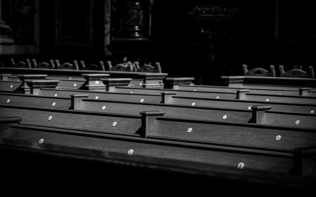 A serene black and white image of church pews in soft light, evoking a peaceful and contemplative atmosphere.