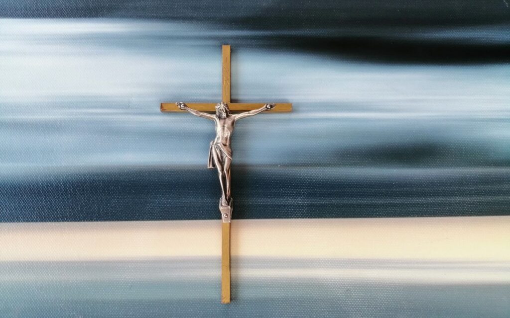 Metal crucifix against a blurred abstract blue and white background, symbolizing faith and spirituality.
