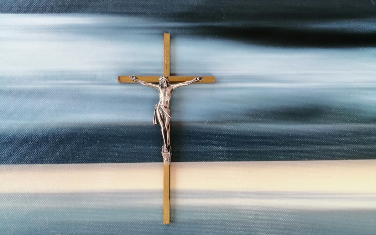 Metal crucifix against a blurred abstract blue and white background, symbolizing faith and spirituality.
