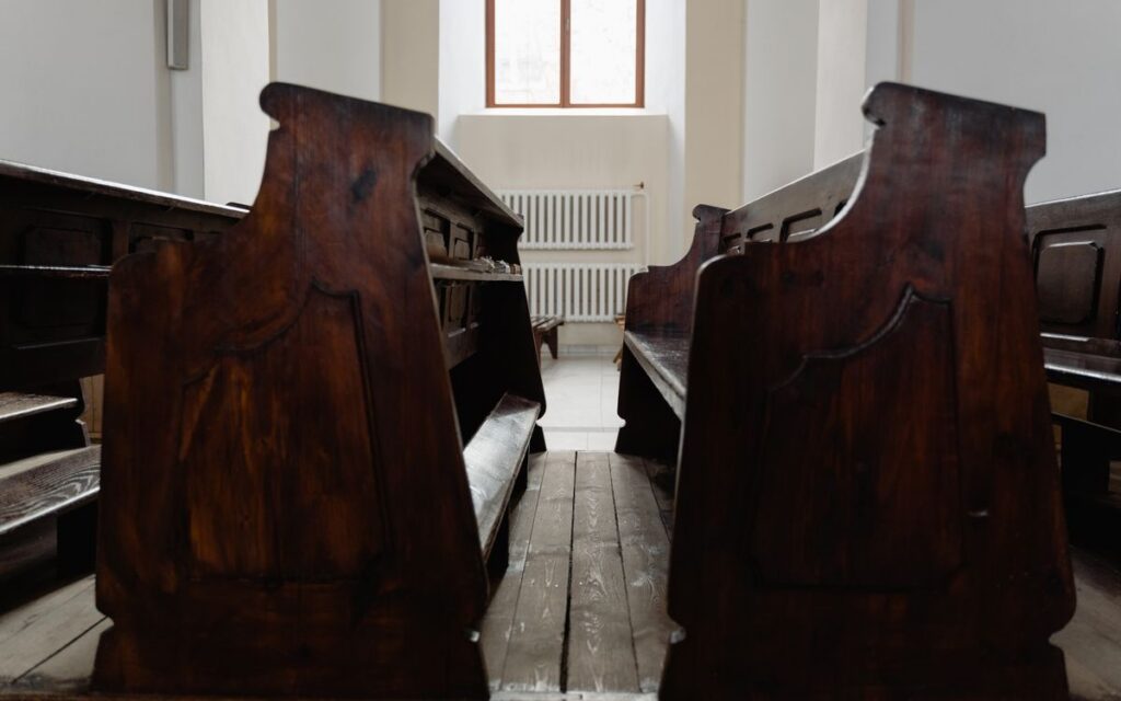 A serene church interior featuring wooden pews and warm natural light streaming through a window.