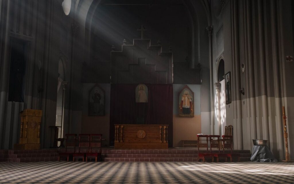 A serene church interior illuminated by sunlight, featuring an altar and religious art.
