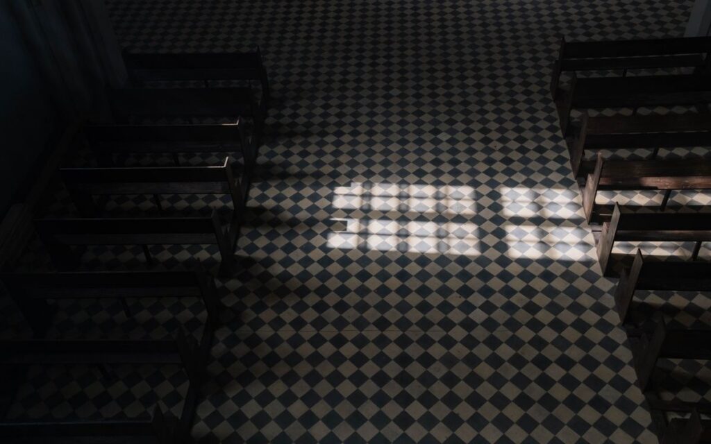Sunlight casts geometric patterns on a church's tiled floor viewed from above.