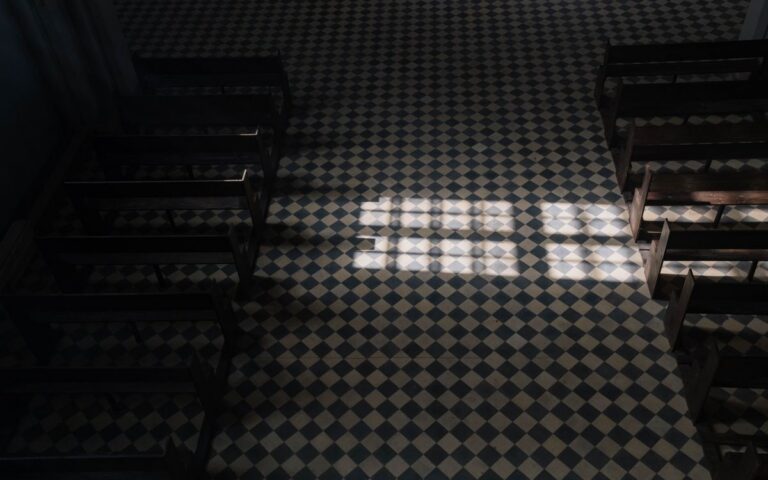 Sunlight casts geometric patterns on a church's tiled floor viewed from above.