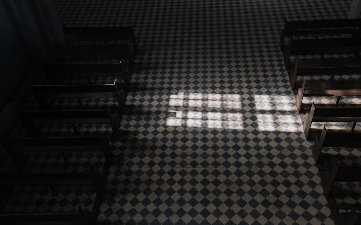 Sunlight casts geometric patterns on a church's tiled floor viewed from above.