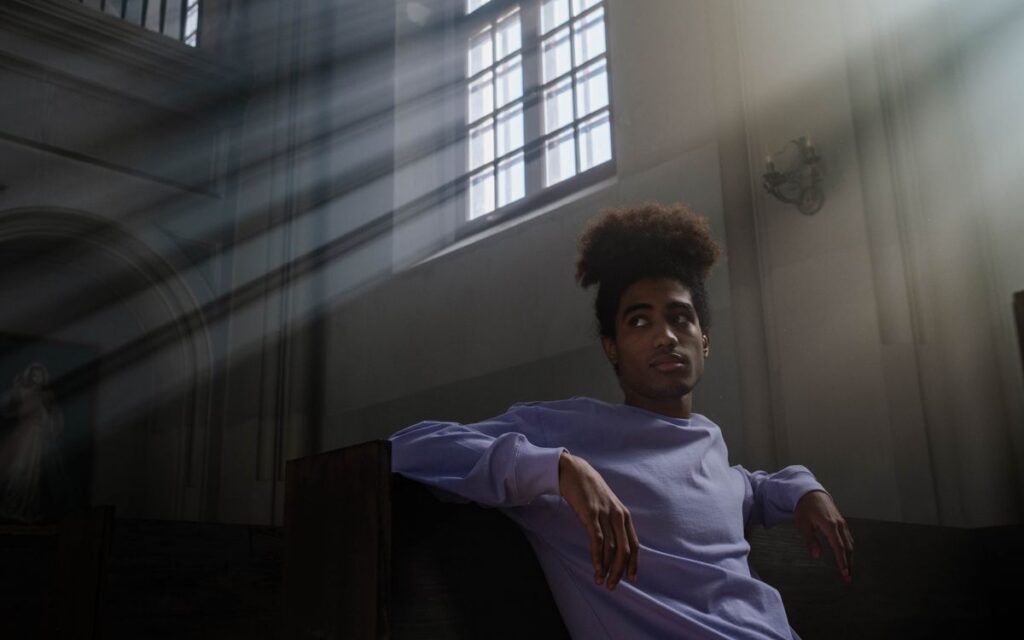 Serene scene of a man in a church with sunlight streaming through windows, creating a peaceful atmosphere.