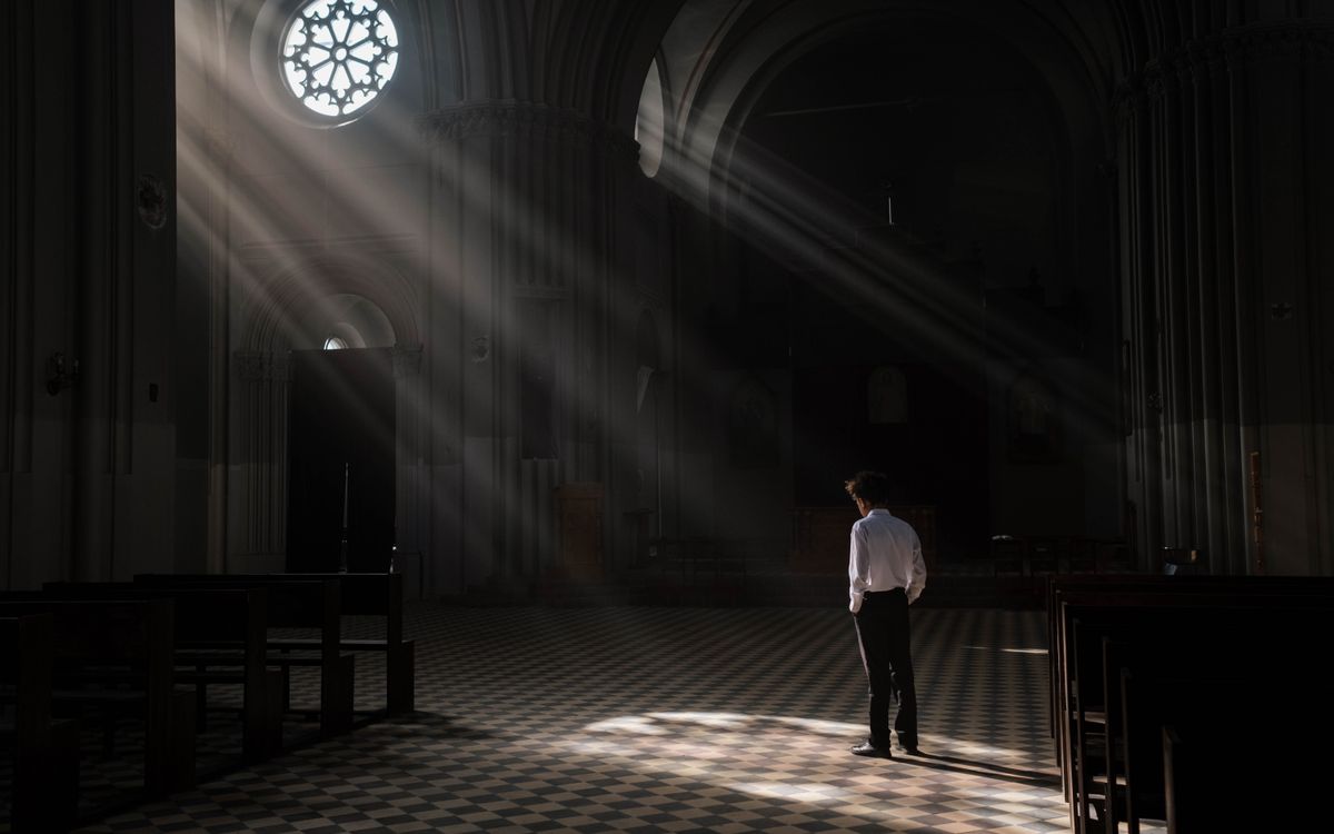 Person standing in a sunlit church interior with dramatic rays through a window.