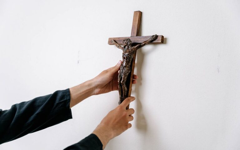 Close-up image of hands placing a wooden crucifix on a white wall emphasizing spirituality.