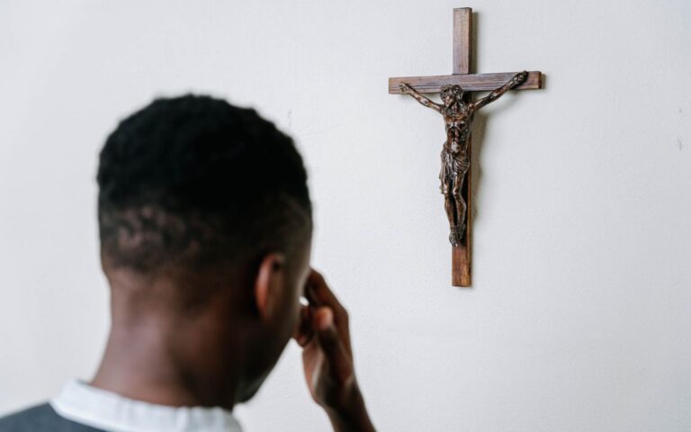 A person praying before a wooden crucifix on a plain wall, symbolizing faith and devotion.
