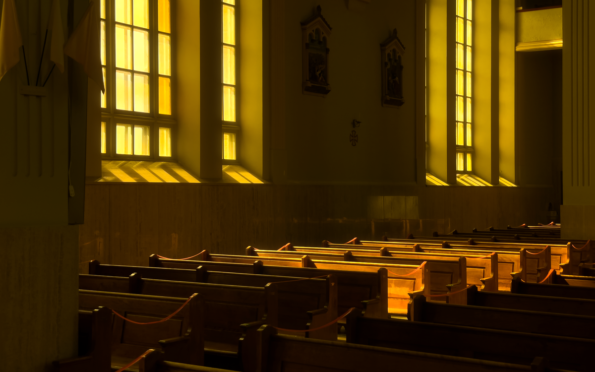 Sunlit church interior highlighting rows of wooden pews and stained glass windows.