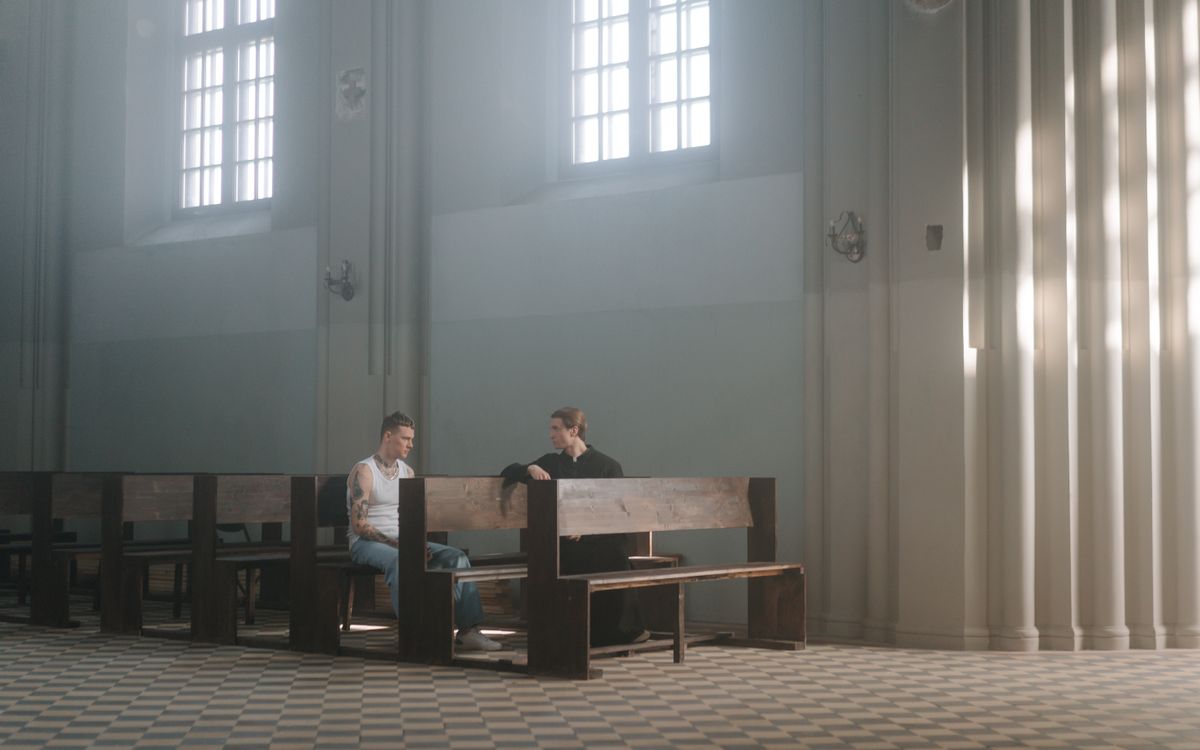 Two men engage in a quiet conversation in a peaceful church interior with light streaming in.