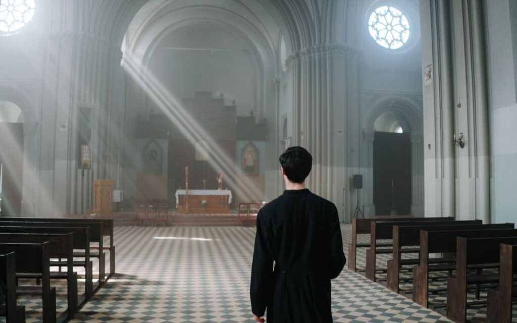 A priest standing inside a cathedral with sunlight streaming through the windows.