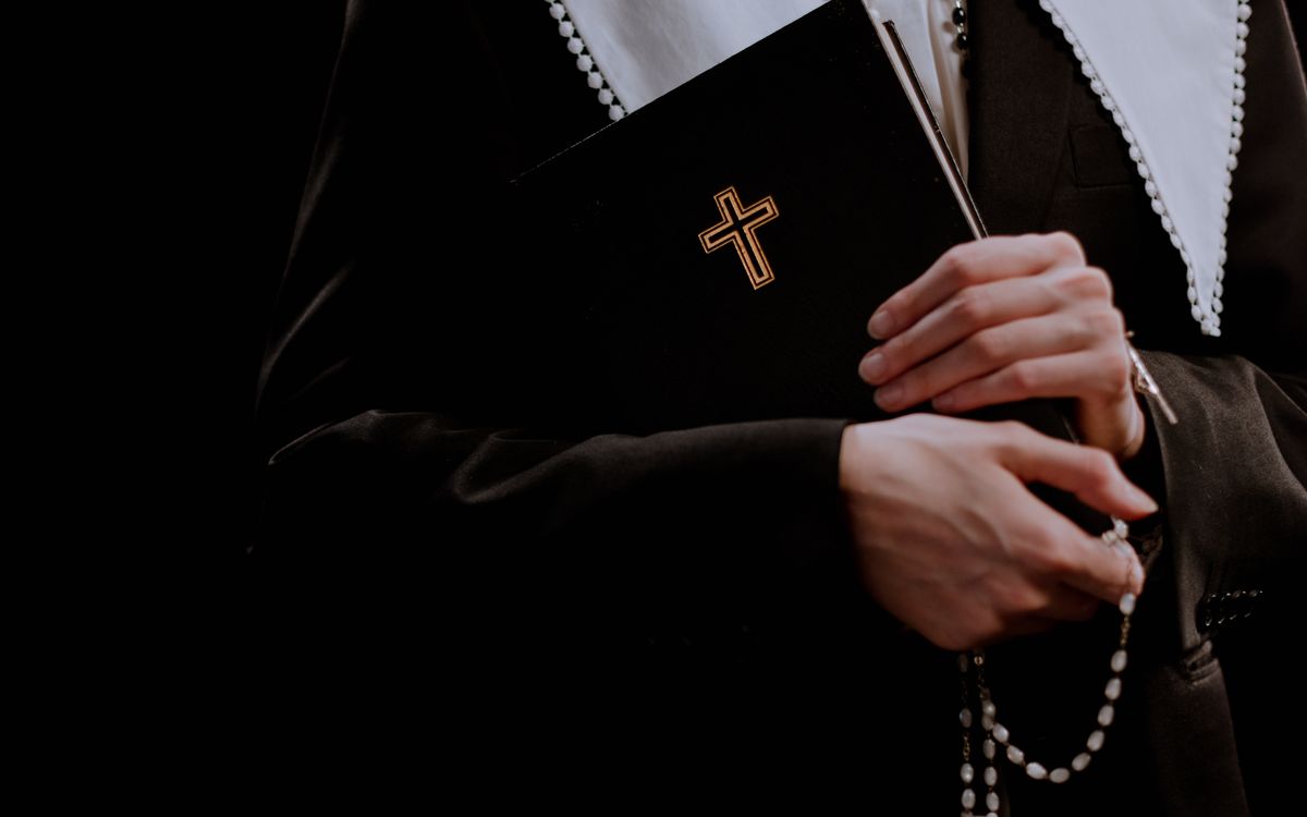 Close-up of a nun holding a Bible with a cross and rosary beads, symbolizing faith.
