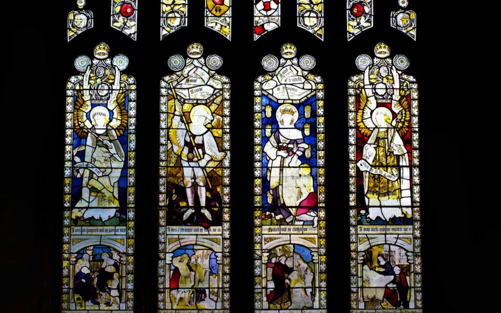 Intricate stained glass windows depicting religious scenes in an English cathedral.