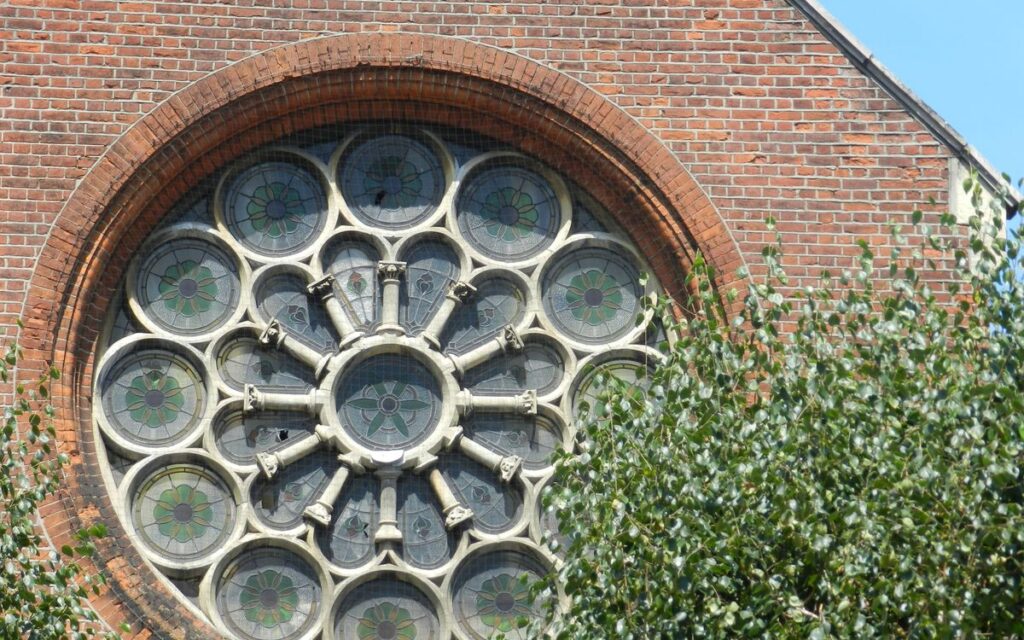 Detailed view of a historic church's rose window framed by a brick wall and greenery.