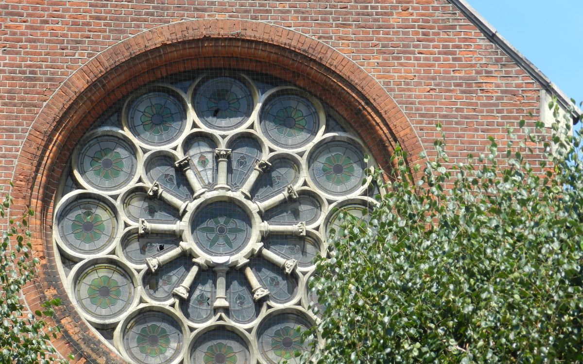 Detailed view of a historic church's rose window framed by a brick wall and greenery.