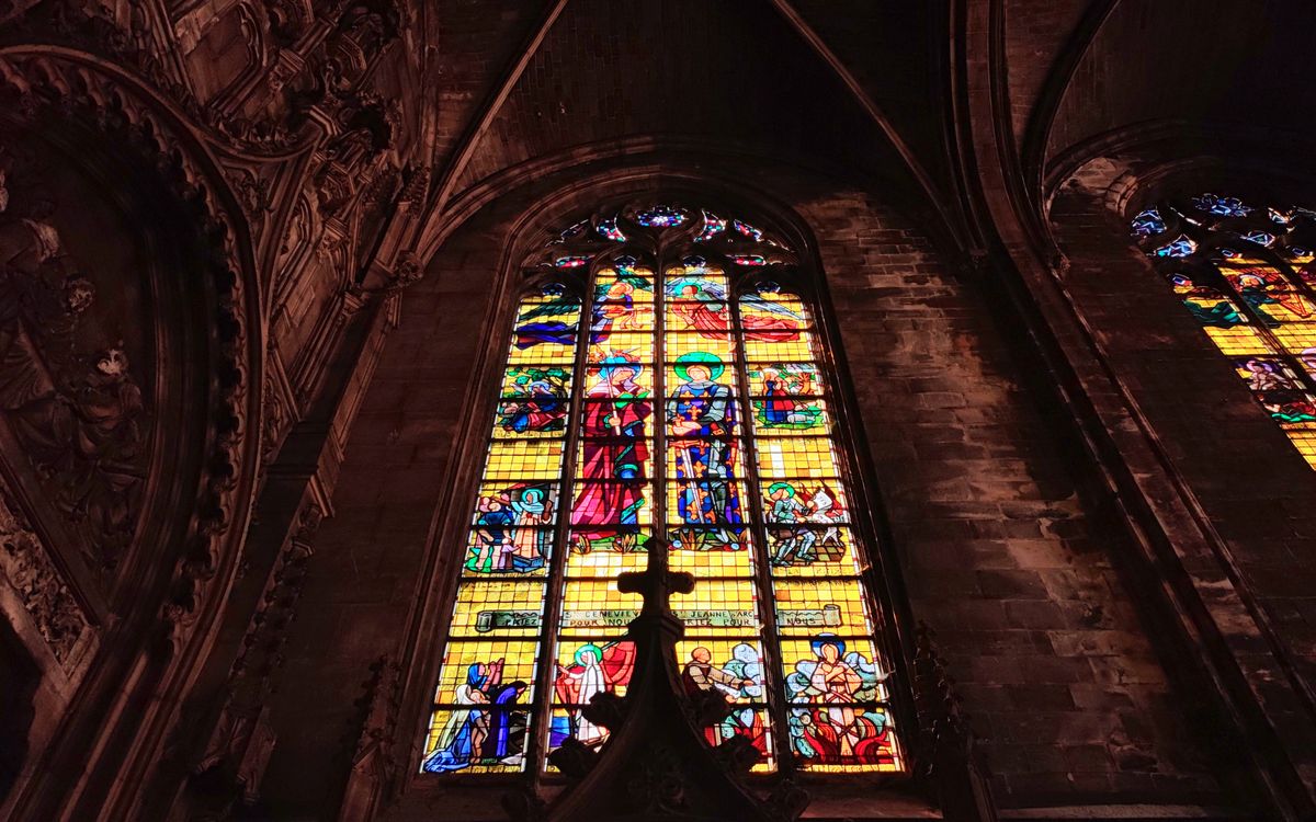 Interior view of a Gothic cathedral with vibrant stained glass windows depicting religious scenes.