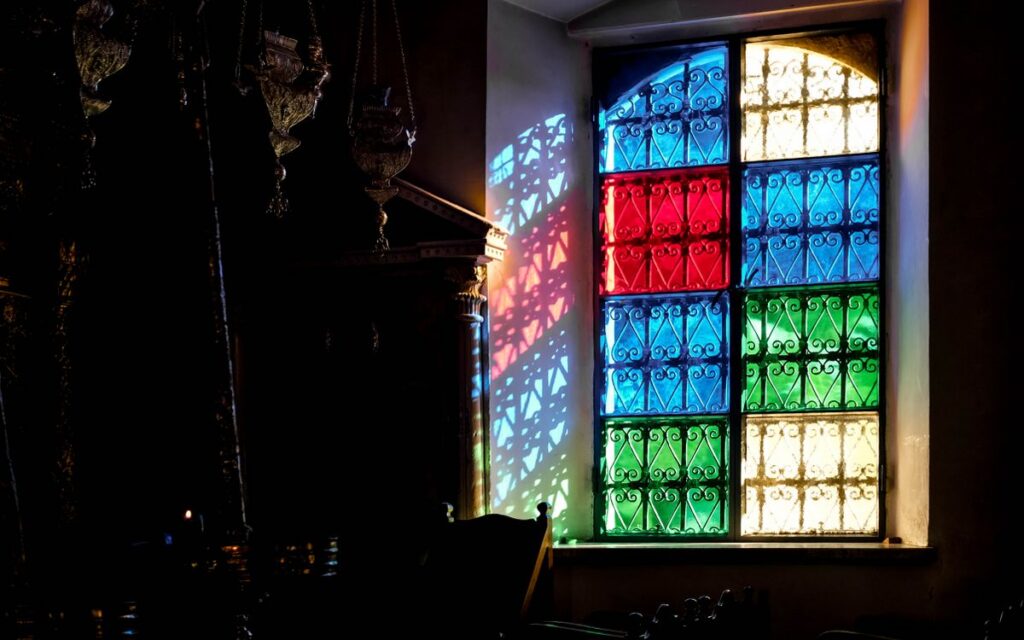 Colorful stained glass window casting vibrant shadows in a dimly lit room.