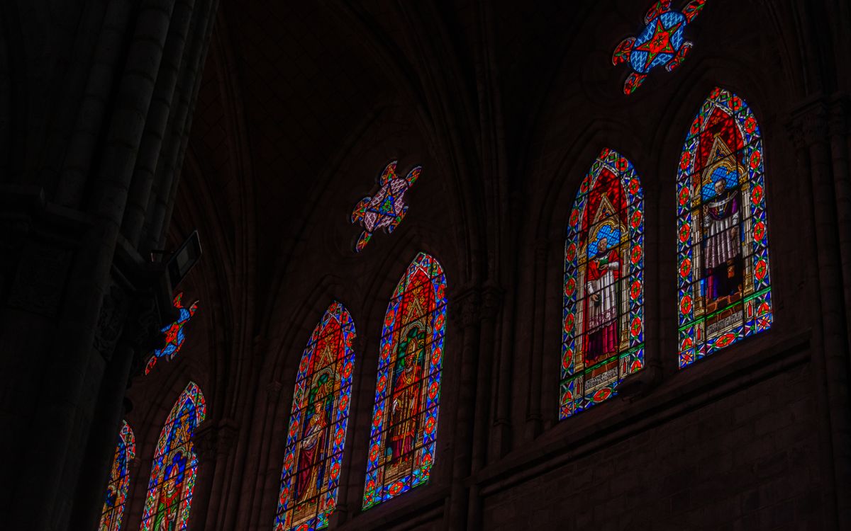 Intricate stained glass windows inside a Gothic cathedral, depicting religious figures and vibrant art.