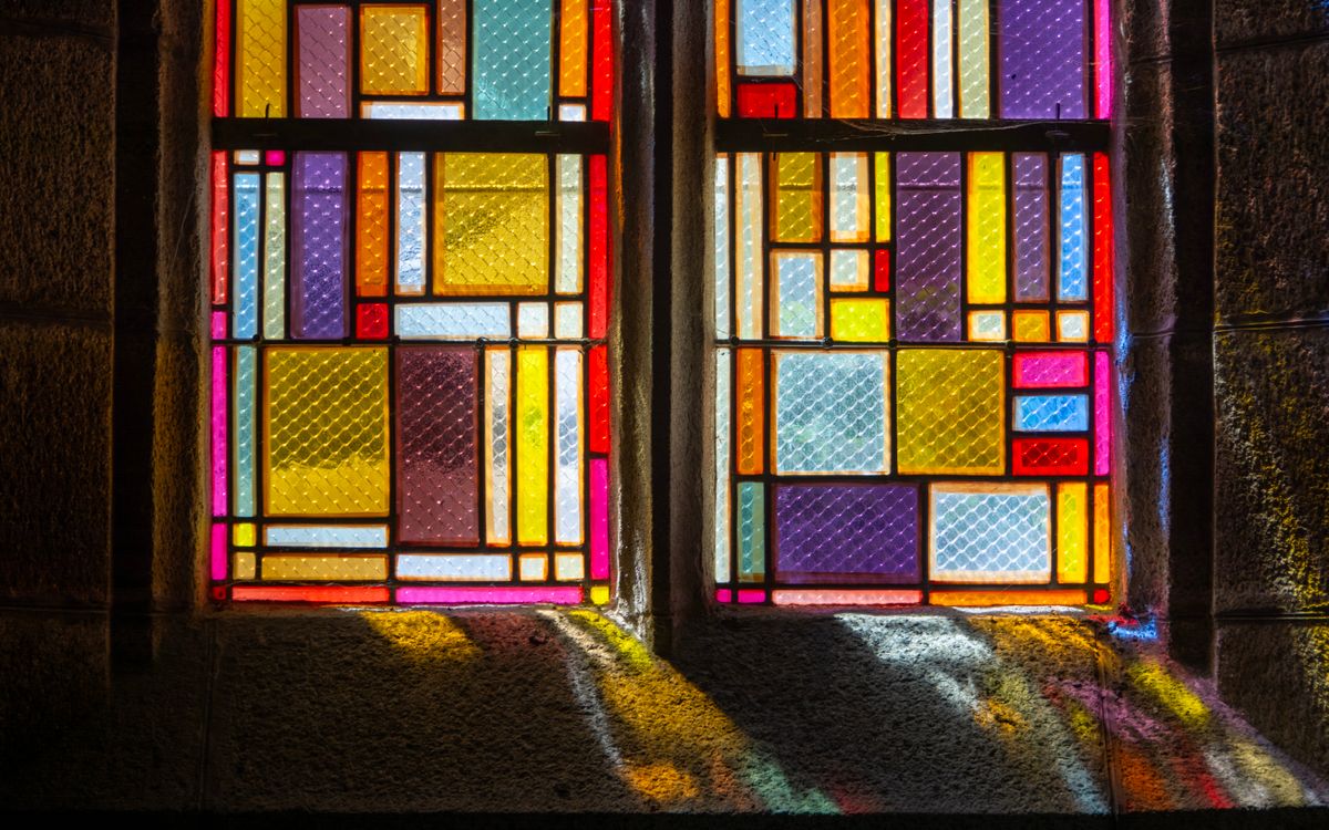 Close-up of a vibrant stained glass window with colorful geometric patterns, casting light indoors.