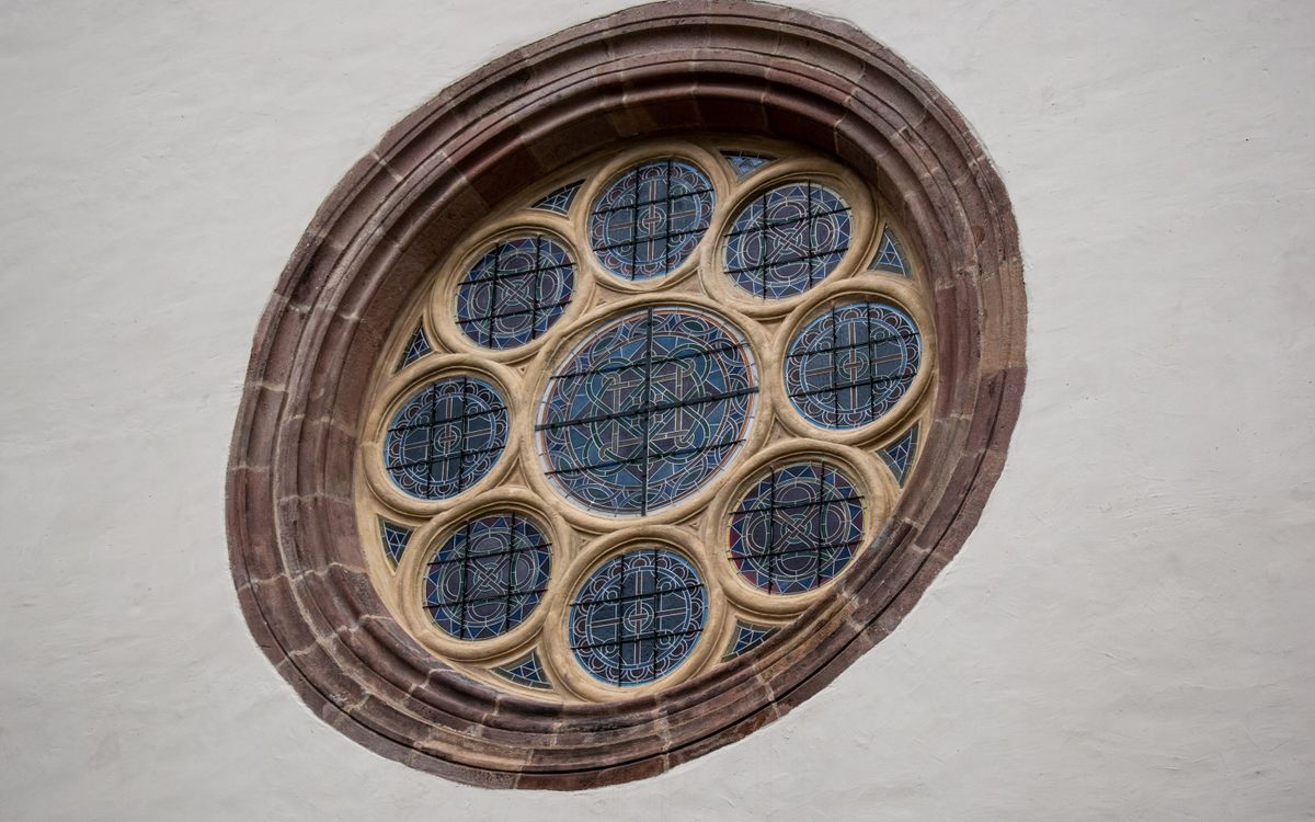 Close-up of a circular stained glass window with intricate patterns in a historic building.