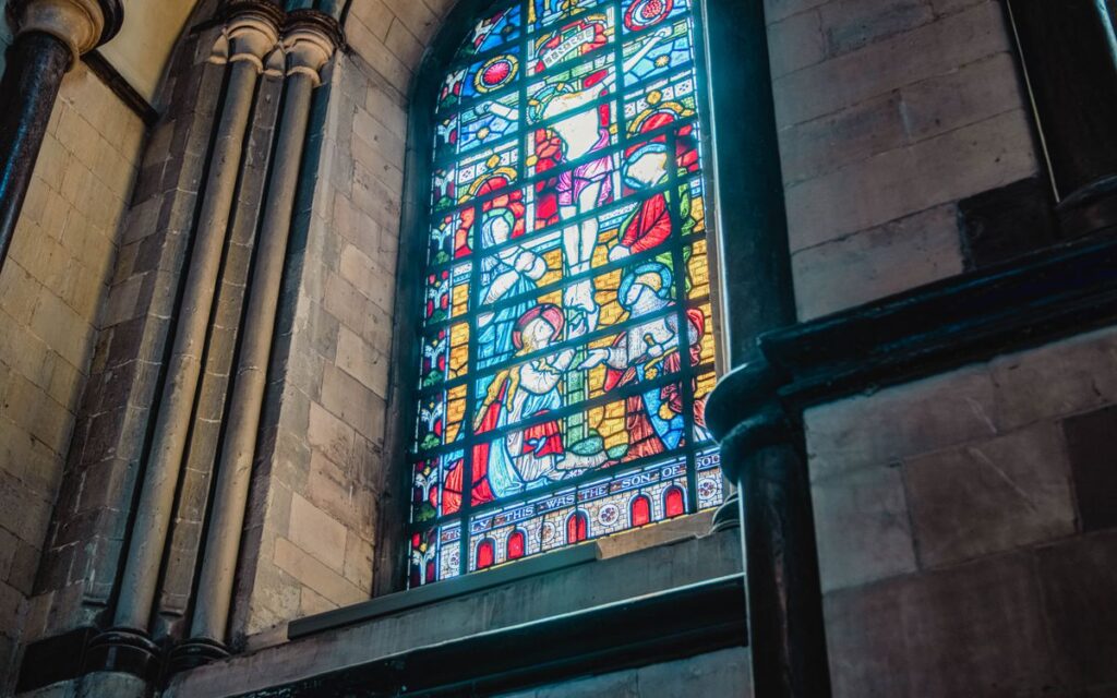 Colorful stained glass window inside a historic cathedral, showcasing religious artwork.