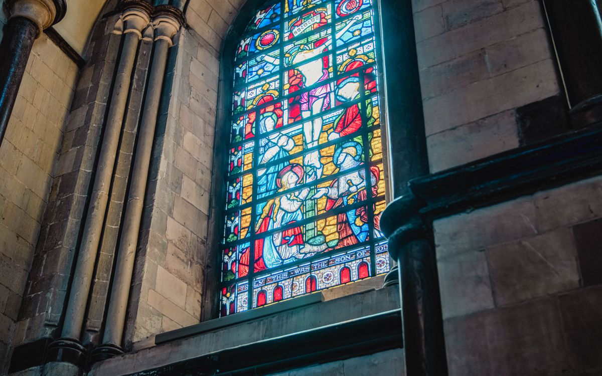 Colorful stained glass window inside a historic cathedral, showcasing religious artwork.