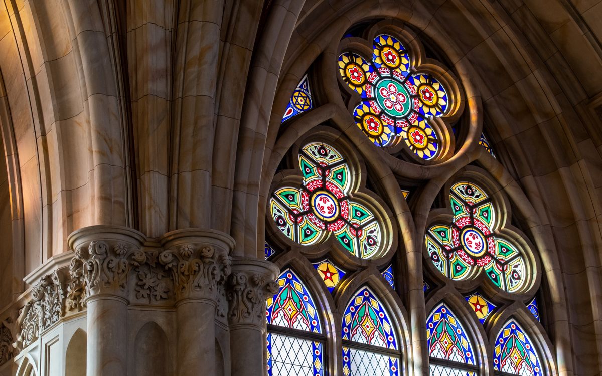 Intricate Gothic-style stained glass window with vibrant colors and ornate patterns inside a cathedral.