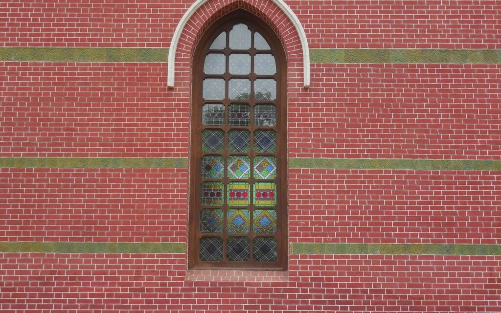 Elegant stained glass window set in red brick wall with arched design.