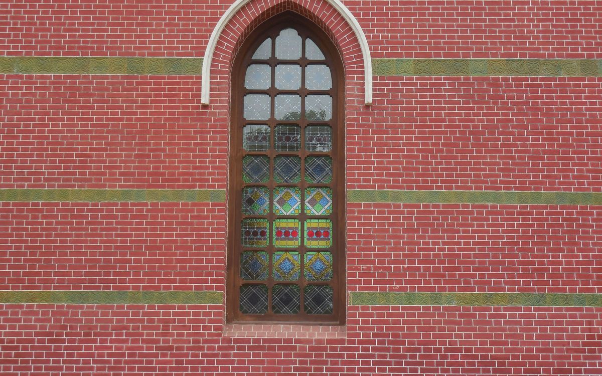 Elegant stained glass window set in red brick wall with arched design.