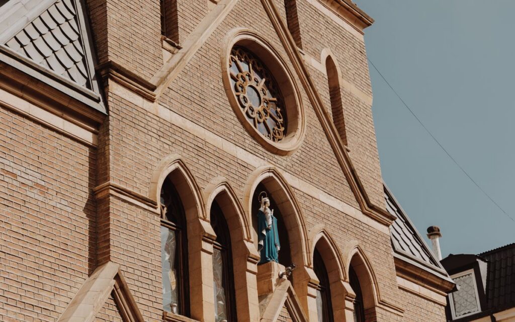 Close-up of a Gothic church facade featuring brickwork, stained glass windows, and religious statues.