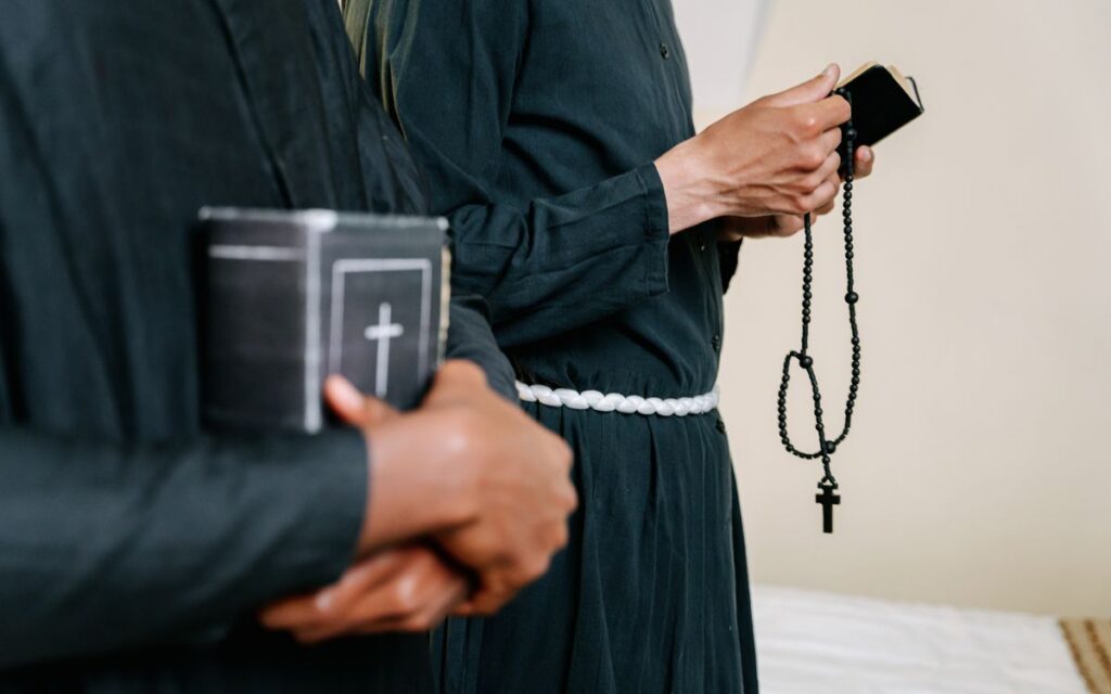 Clergy members in religious robes holding bibles and rosary beads, symbolizing faith.