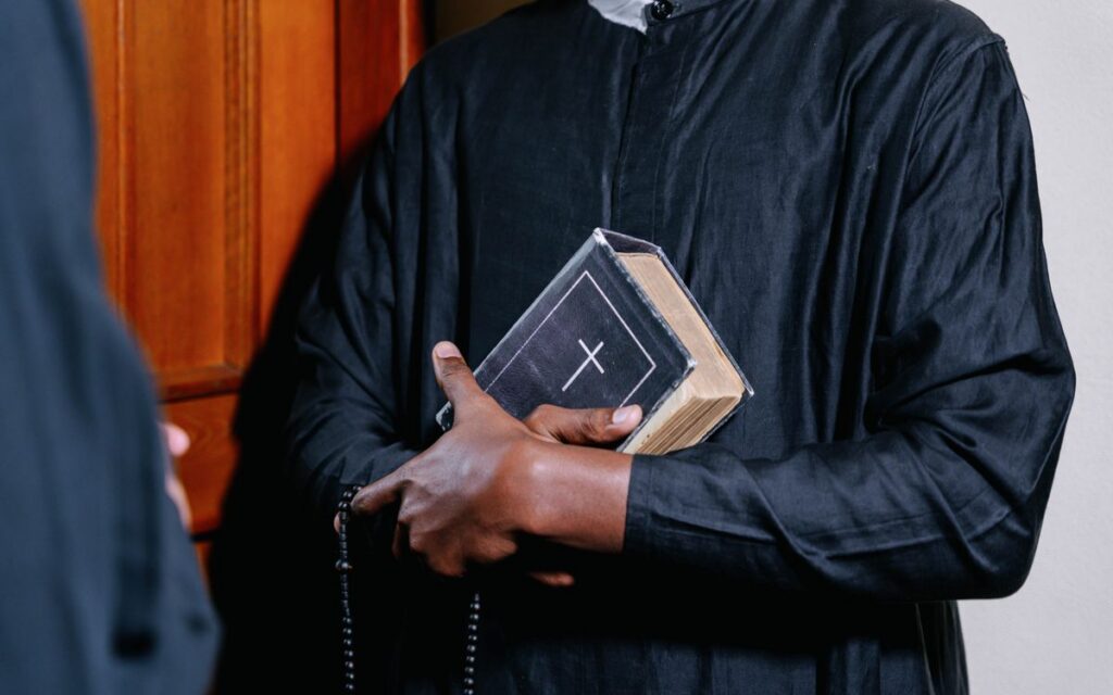 Close-up of a priest holding a Bible and rosary beads, symbolizing faith and spirituality.