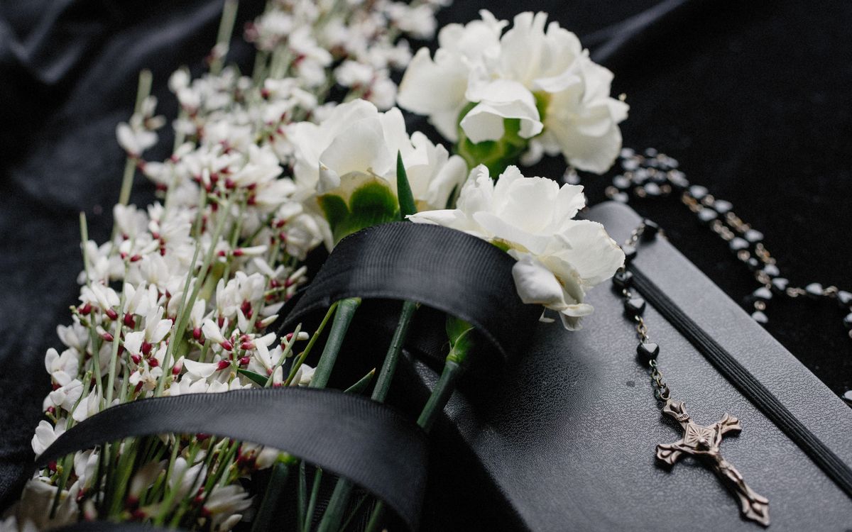 Close-up of white flowers and rosary on dark cloth, symbolizing mourning and spirituality.