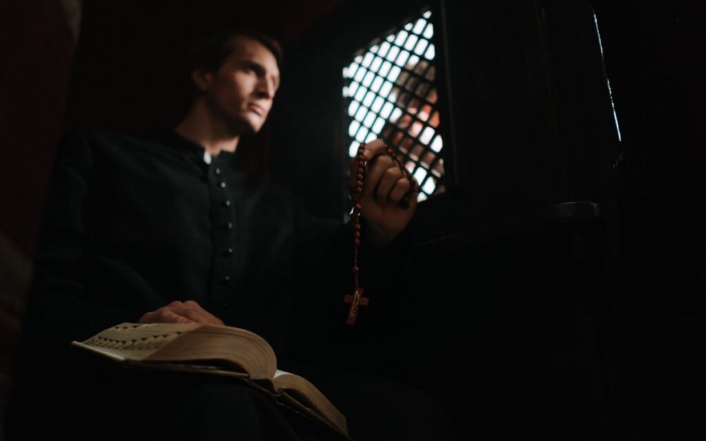 A priest holding prayer beads in a confessional booth, offering spiritual guidance.