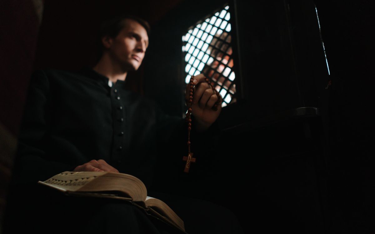 A priest holding prayer beads in a confessional booth, offering spiritual guidance.